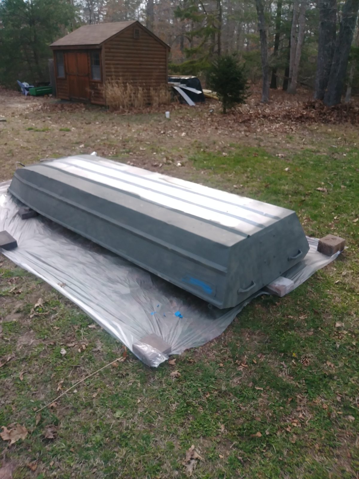Hull tarped on blocks with primer coat drying, shed in the background